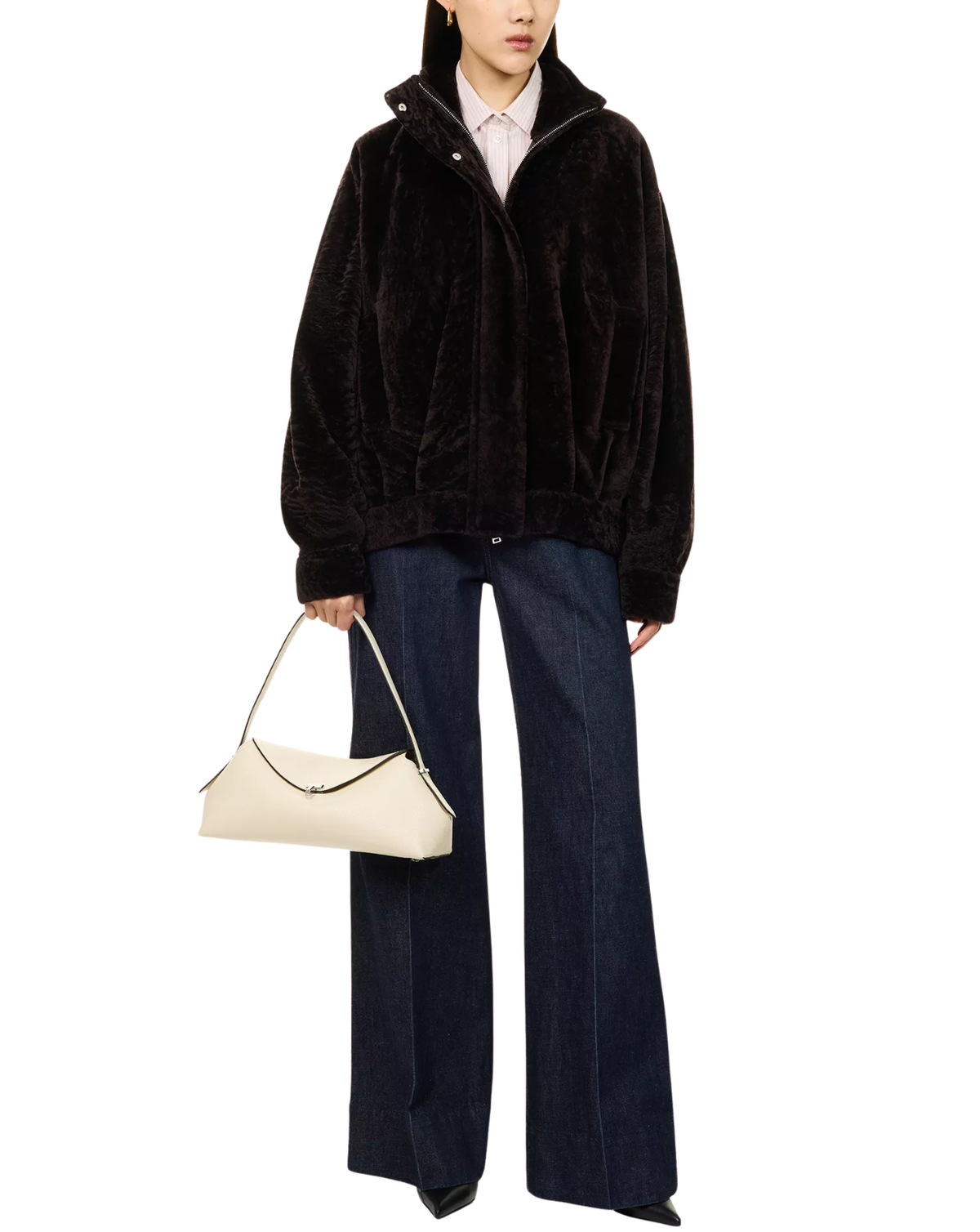 A model wearing a black plush fleece zip-up jacket over a white collared shirt, paired with dark blue wide-leg jeans and holding a cream-colored handbag, set against a plain white background.