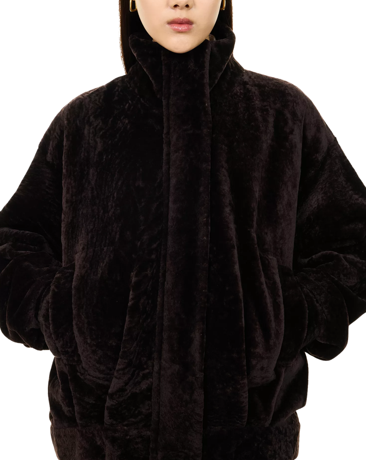 A close-up of a person wearing an oversized black plush faux-fur hooded jacket against a plain white background.