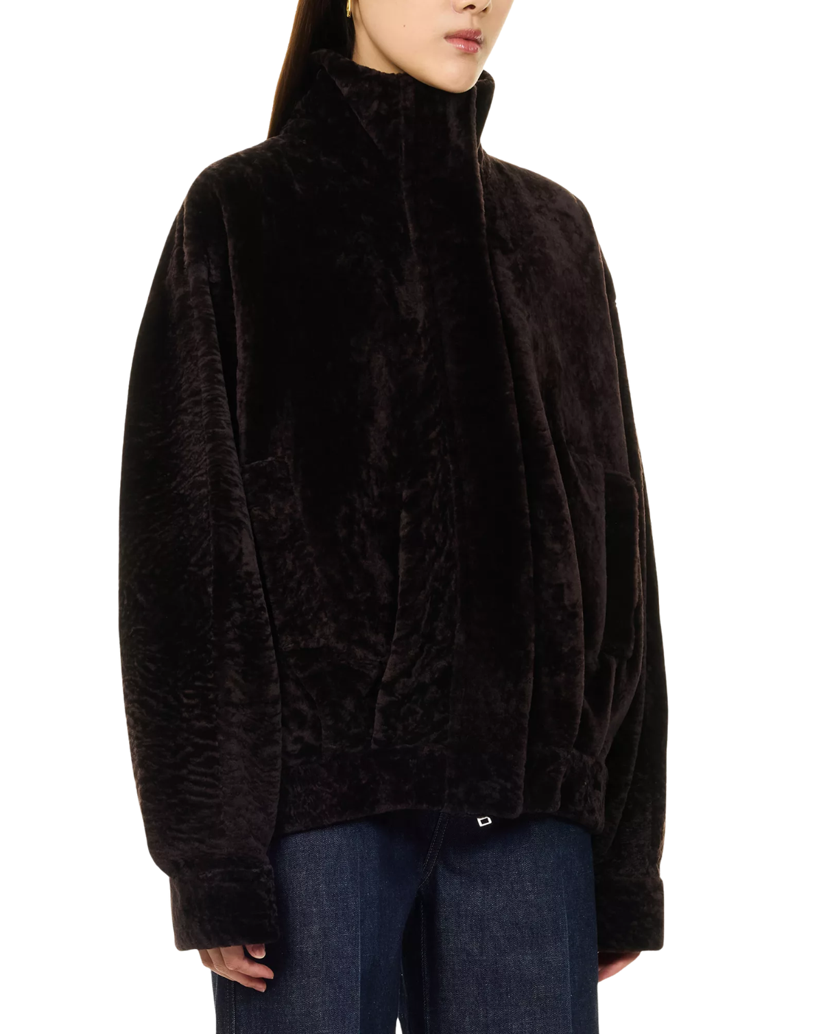 A model wearing a dark brown plush faux fur jacket with a high stand-up collar and drawstring details, paired with blue jeans against a plain white background.