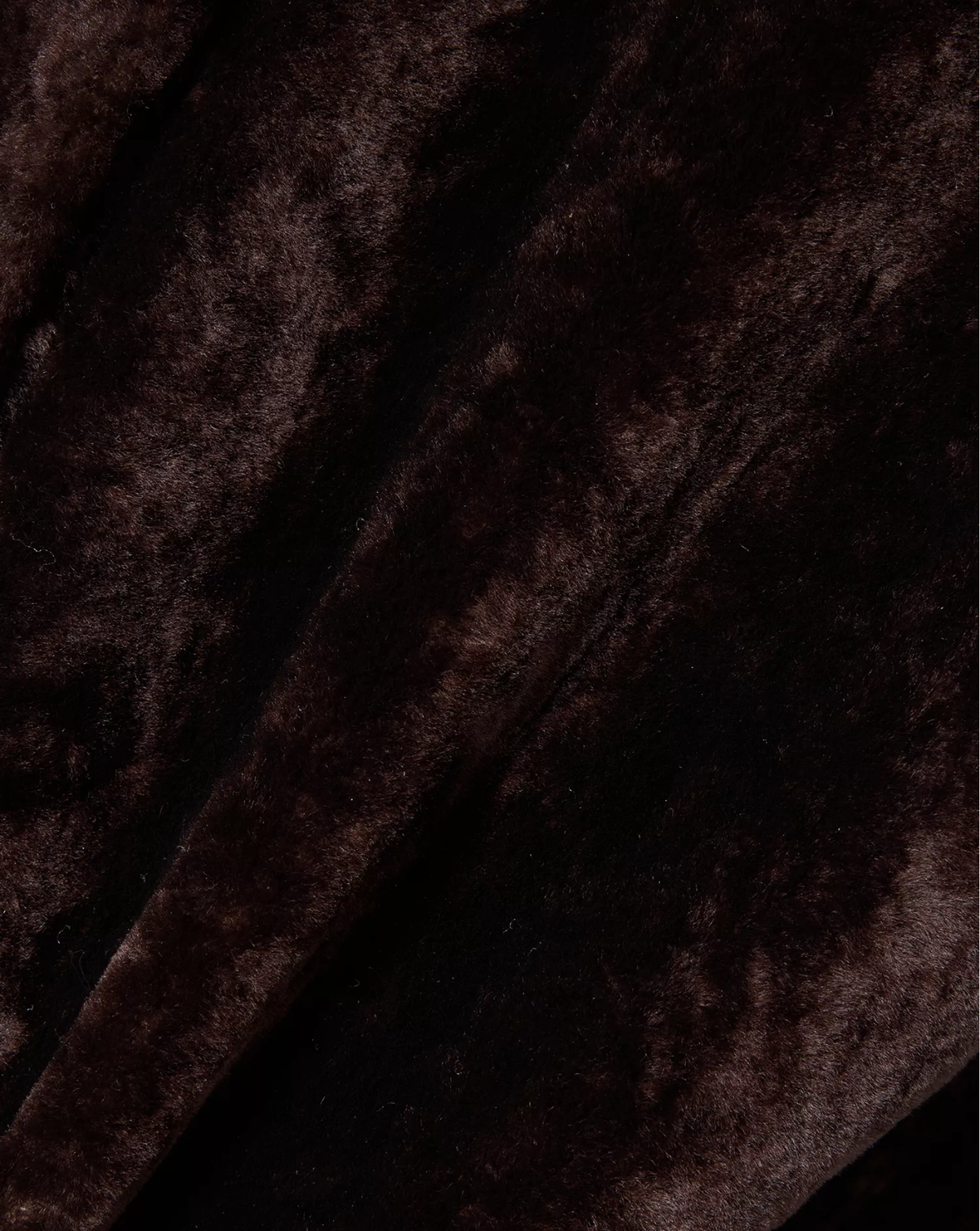 A close-up of dark brown plush velvet fabric with soft diagonal folds and a rich, velvety texture.