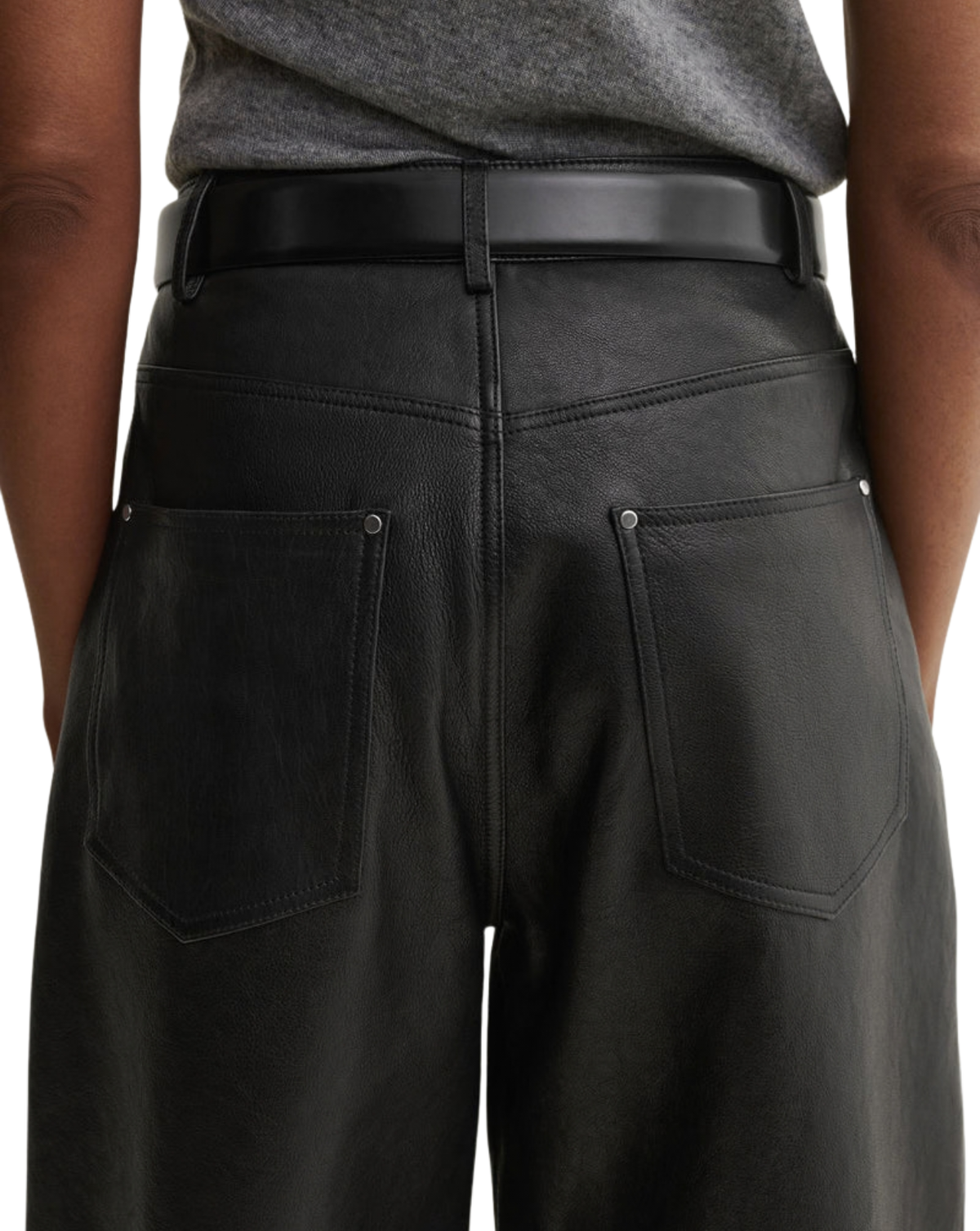 Close-up back view of a person wearing black wide-leg leather pants with a black belt, a gray top, and dark skin visible on both sides.