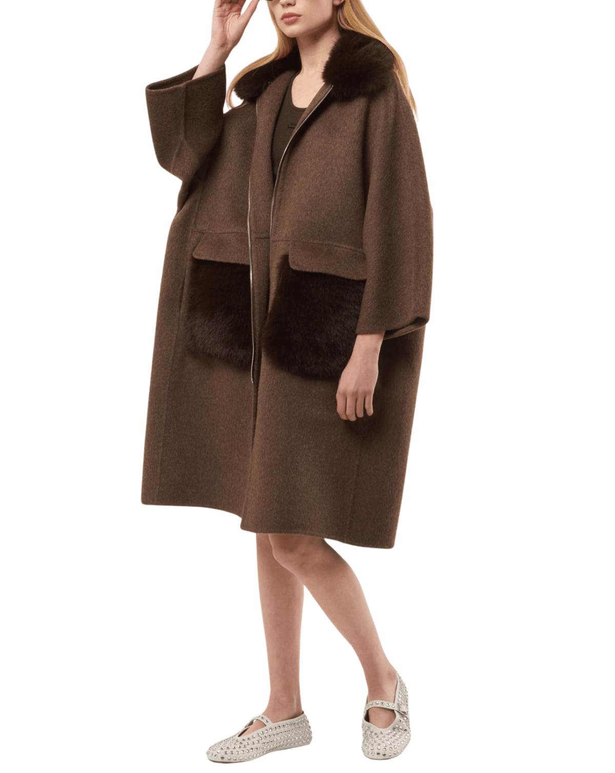A woman models a brown wool coat with dark brown fur trim on the collar and front pockets, paired with white woven shoes, against a plain white background.