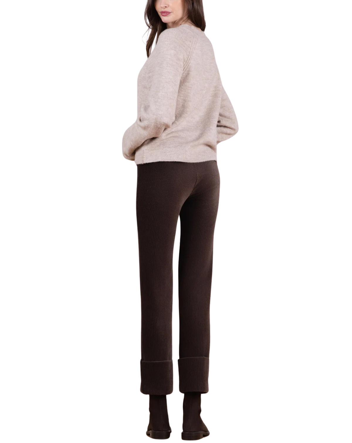 A woman shown from the back wearing a light beige knit sweater and dark brown cropped pants with rolled cuffs, against a plain white background.