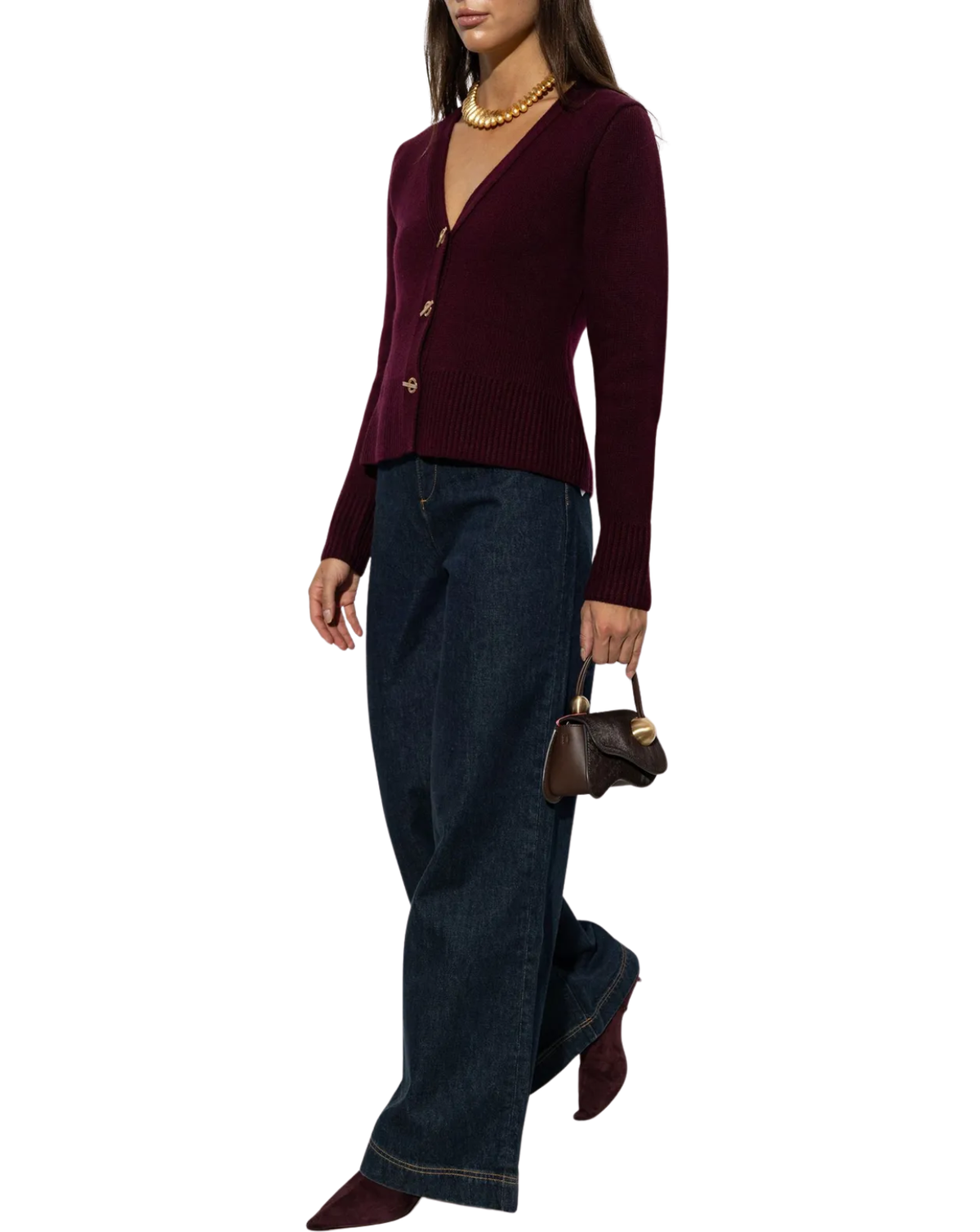 A woman modeling a burgundy knit cardigan with gold buttons, paired with dark blue wide-leg jeans, burgundy pointed-toe heels, a gold necklace, and carrying a small brown handbag against a plain white background.