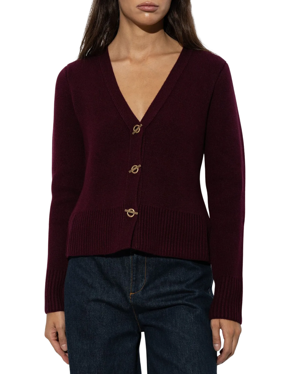 A woman wearing a burgundy knit cardigan with a V-neck and gold-tone circular buttons, paired with dark blue jeans, against a plain white background.