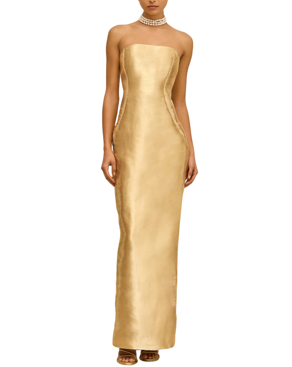 A model wearing a strapless, floor-length gold gown with a structured corset-style bodice and draped side details, paired with a pearl choker and brown sandals, set against a plain white background.