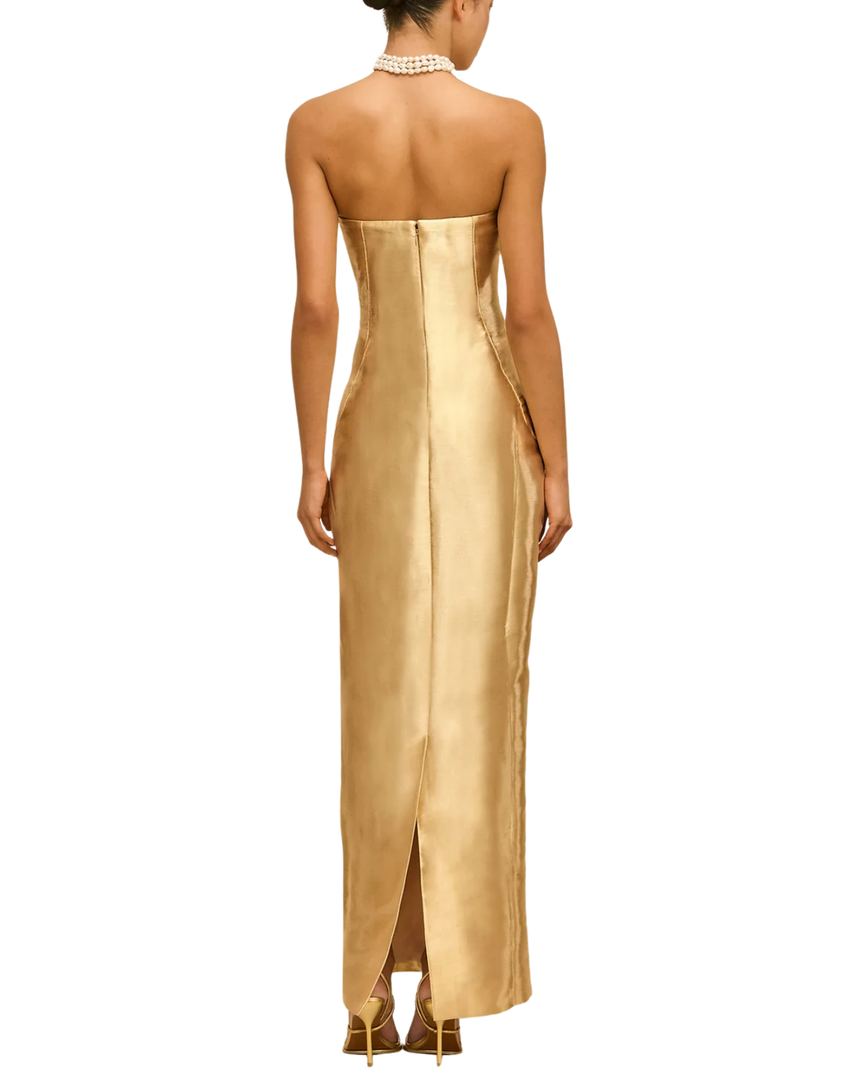 A woman viewed from the back wearing a strapless metallic gold maxi dress with a fitted silhouette and a front slit, paired with gold heels and a pearl choker against a plain white background.