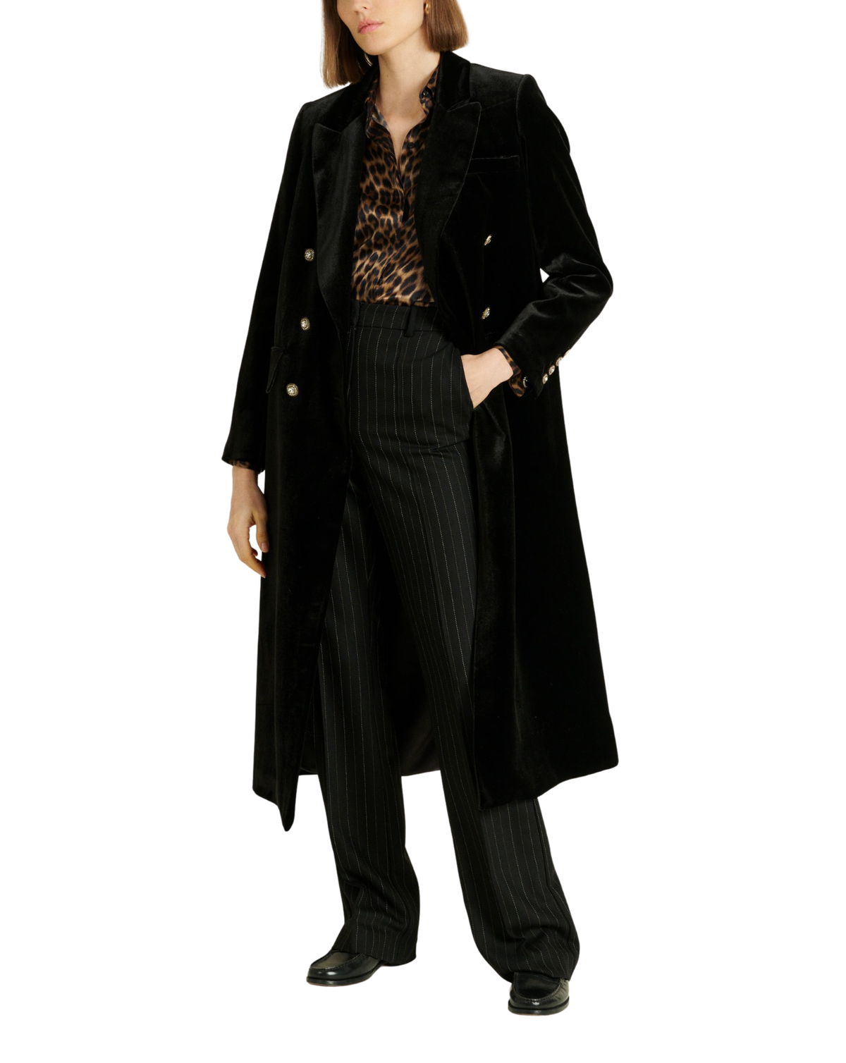 A model wearing a long black velvet double-breasted coat over a leopard print blouse and black pinstripe trousers, photographed against a solid white background.
