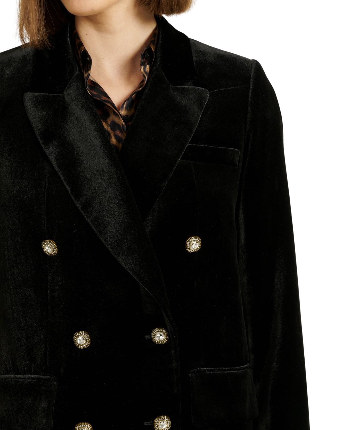 A close-up of a model wearing a black velvet double-breasted blazer with gold buttons, paired with a leopard-print shirt collar, against a white background.