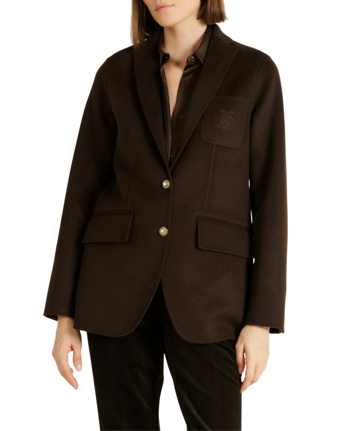 A model wearing a dark brown wool-blend blazer with shawl lapels, gold-tone buttons, flap pockets, and a tonal embroidered crest on the left chest pocket, paired with dark trousers against a plain white background.