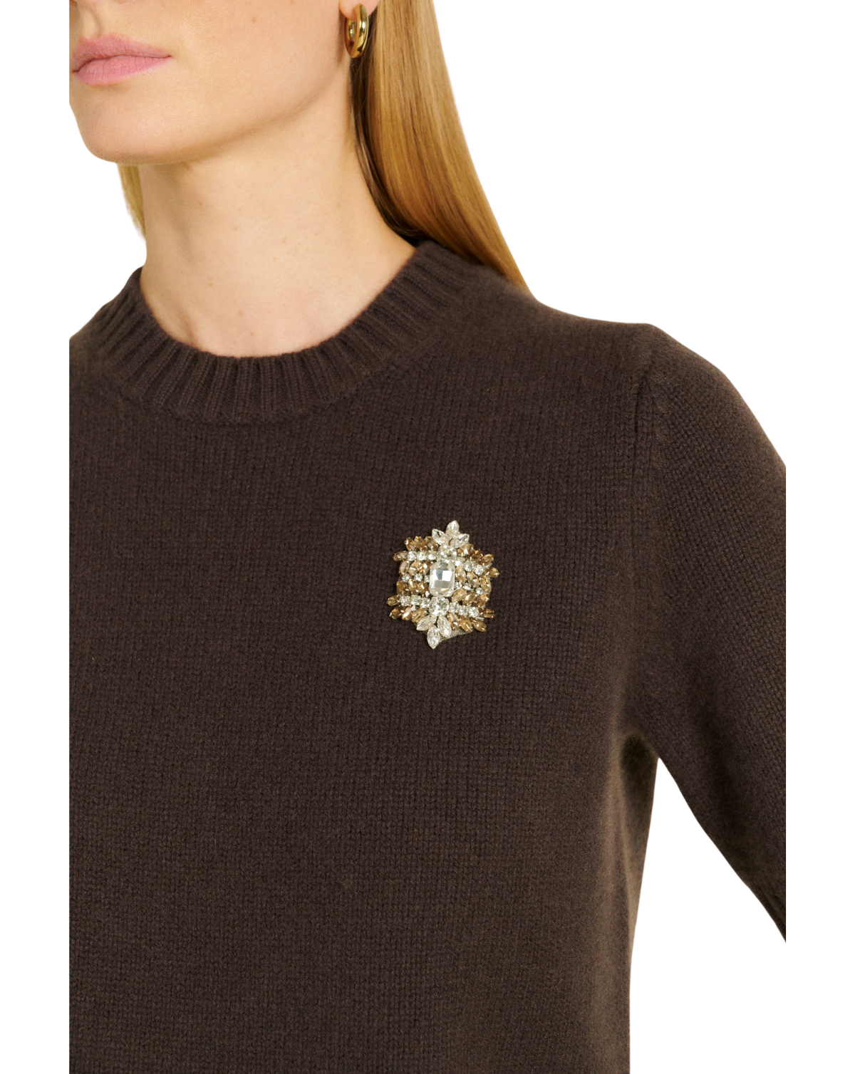 A close-up of a woman wearing a dark brown knit sweater with a decorative brooch featuring clear crystals and gold-toned metal on the left chest.