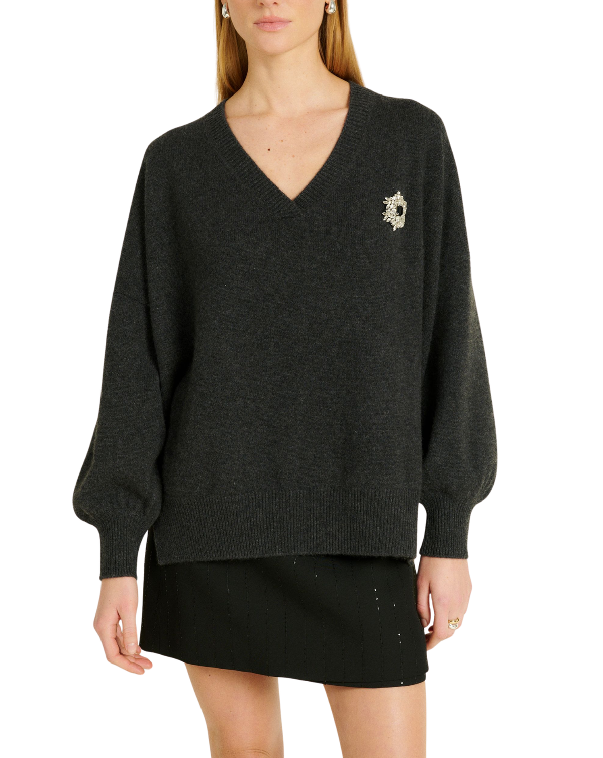 A woman wearing a dark charcoal gray knit sweater with a small gold embroidered logo on the left chest, paired with a black mini skirt, against a plain white background.