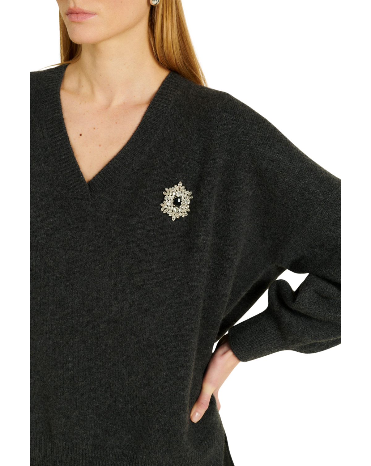 A close-up of a woman wearing a dark charcoal gray V-neck knit sweater with a decorative silver-toned brooch on the chest, set against a plain white background.