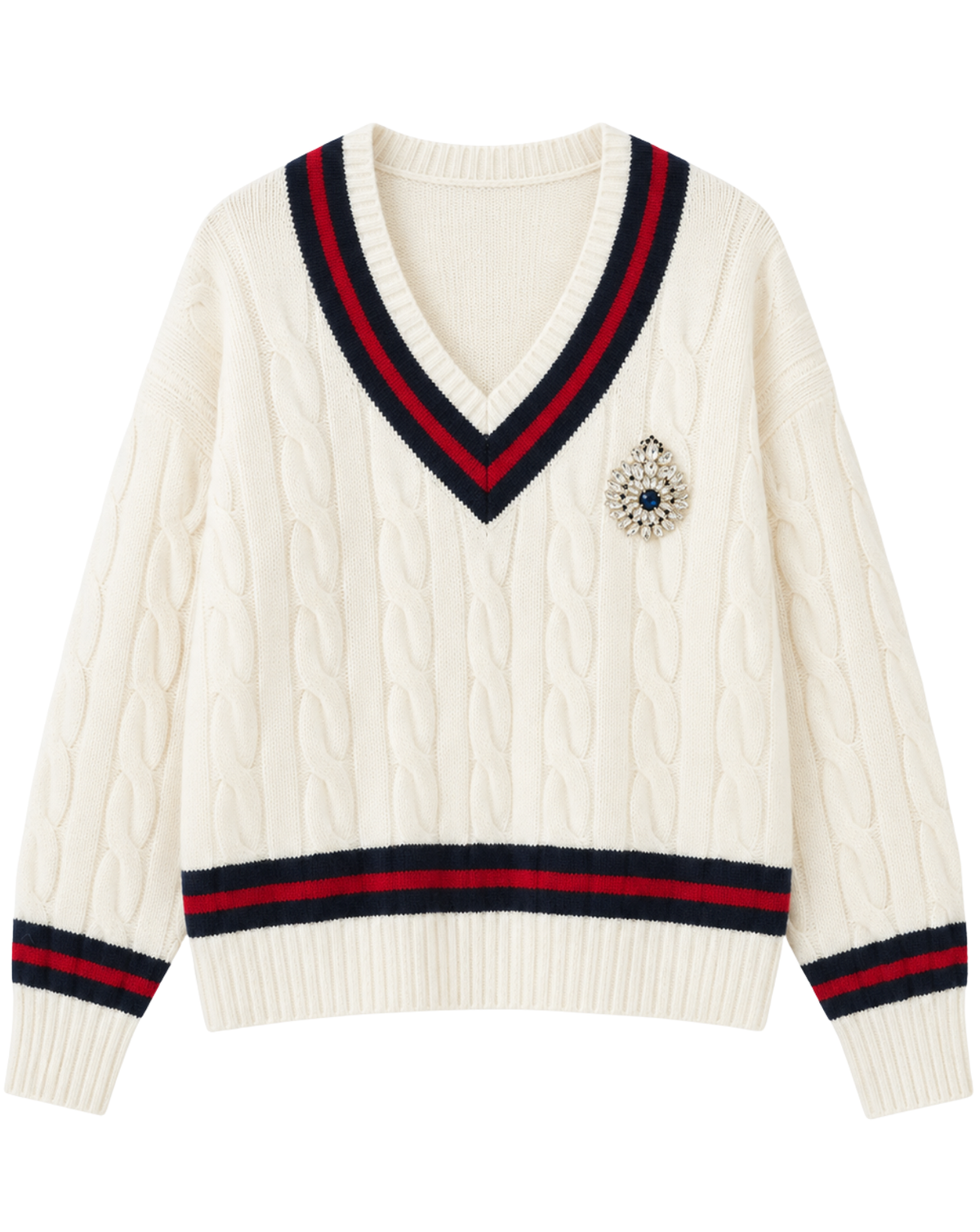 An off-white cable-knit V-neck sweater with navy and red striped trim on the collar, cuffs, and hem, featuring a jeweled crest brooch on the left chest.