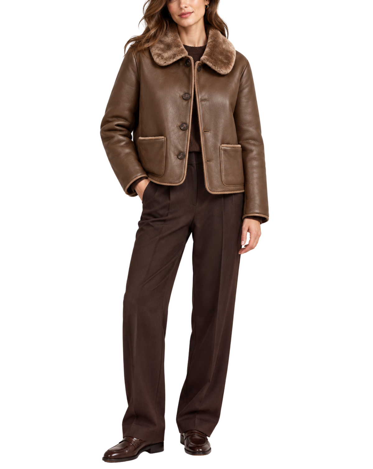 A woman modeling a brown leather jacket with a plush brown fur collar, paired with dark brown trousers and brown shoes, against a plain white background.