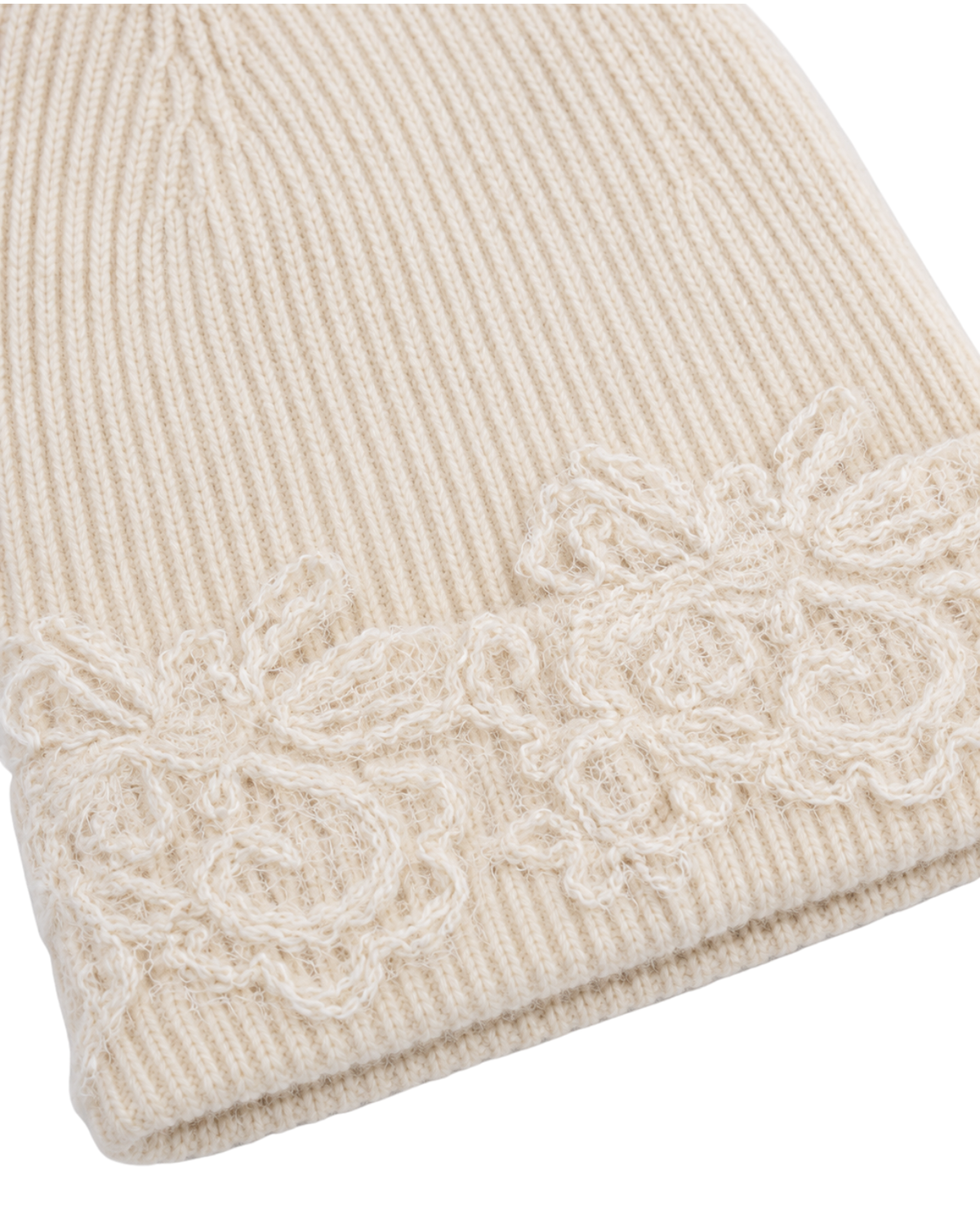 Close-up of a cream-colored ribbed knit beanie with a matching floral lace trim along the folded brim.