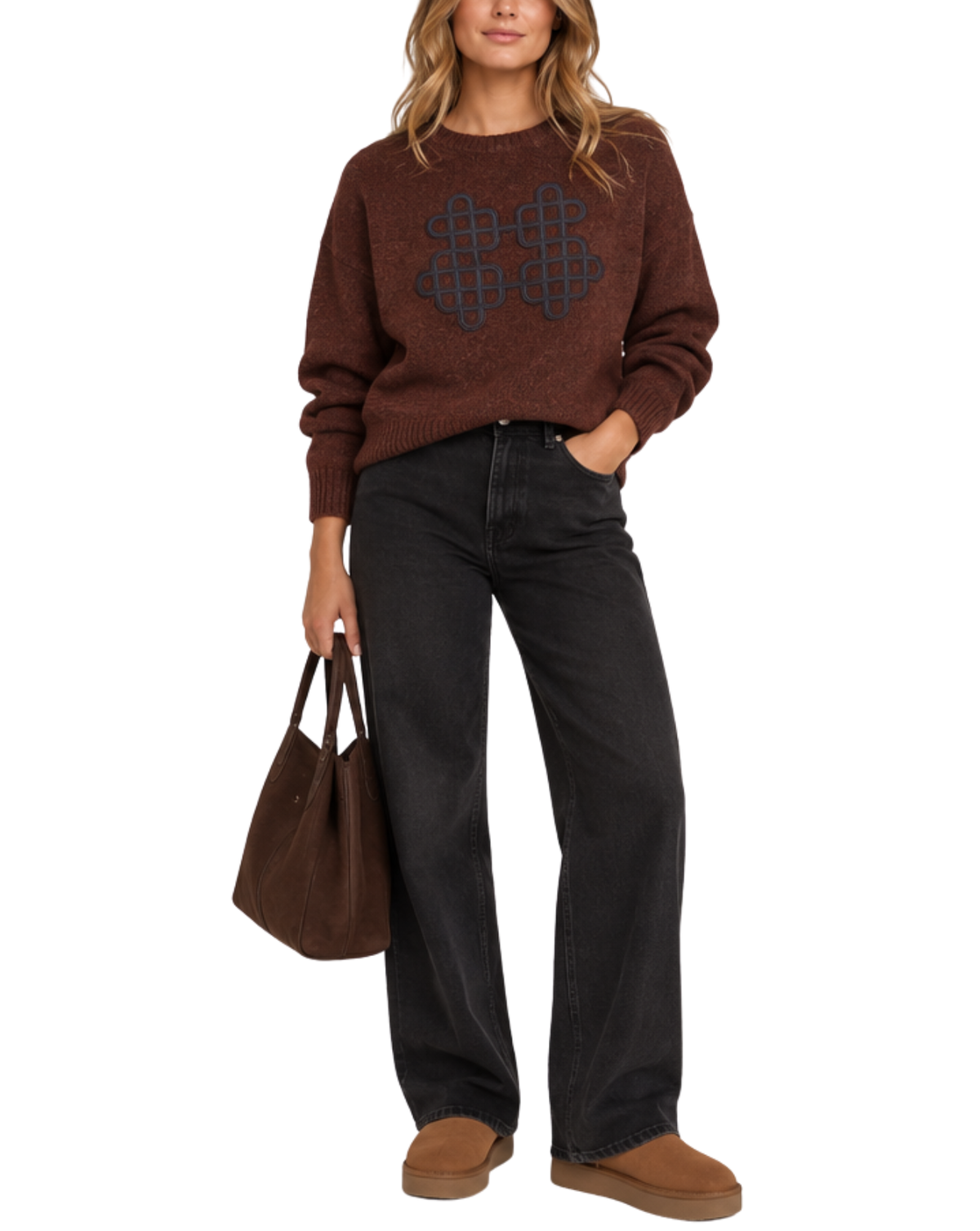 A woman modeling a brown knit sweater with a dark geometric pattern on the chest, paired with black wide-leg jeans, brown suede boots, and holding a brown tote bag against a plain white background.