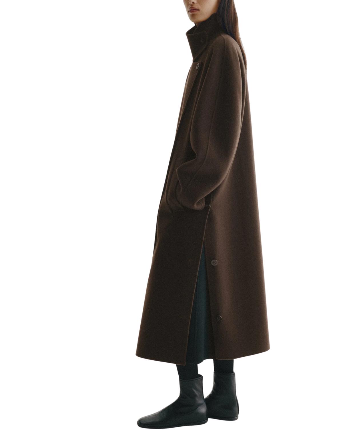 A model shown in profile wearing a long, dark brown wool coat with a high collar, paired with black boots and trousers, against a solid white background.