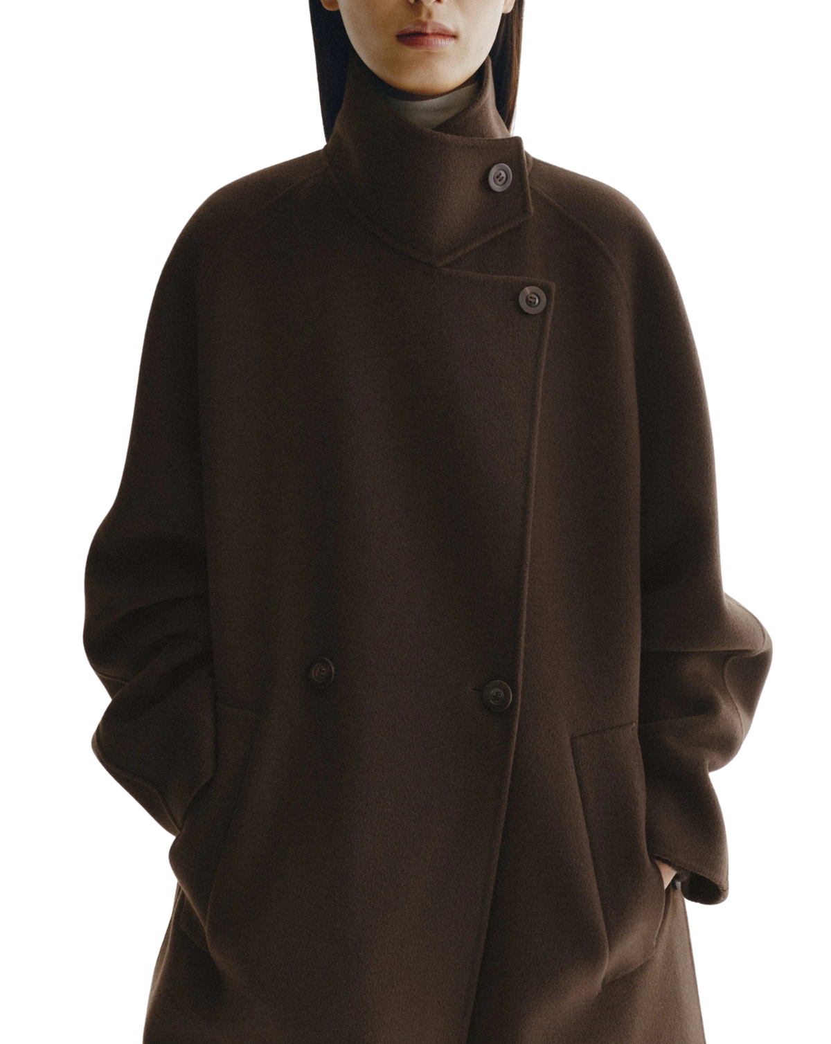 A close-up of a model wearing a dark brown double-breasted coat with a high mock neck collar and asymmetrical button closure, set against a plain white background.