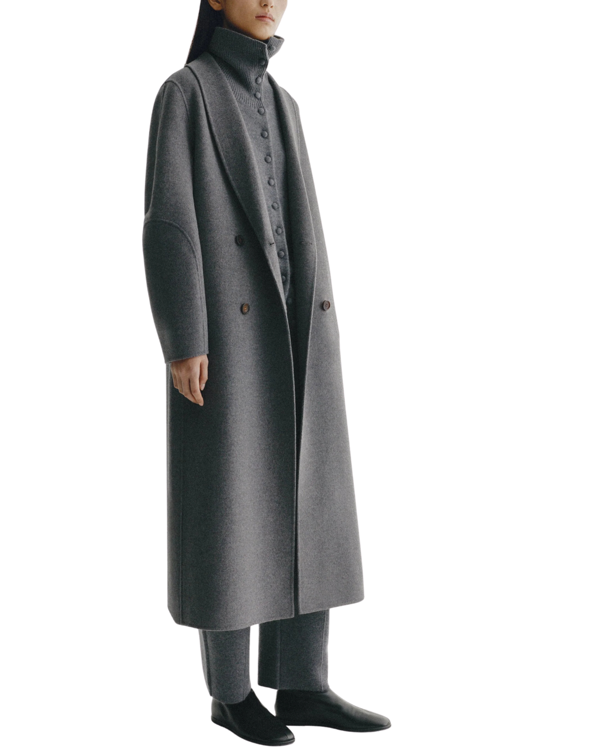 A model wearing a long, double-breasted charcoal gray wool coat with a high structured collar, paired with matching gray trousers and black shoes, set against a plain white background.