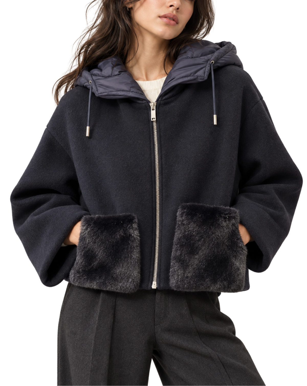 A woman wearing a cropped black zip-up hooded jacket with plush faux-fur trim on the hood lining and front pockets, paired with dark trousers against a plain white background.