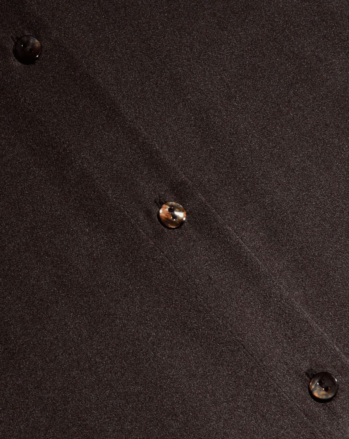 Close-up of a dark brown textured fabric with three iridescent buttons spaced diagonally along the front.