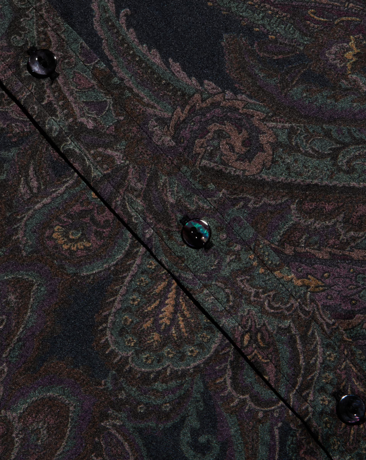 Close-up of a dark paisley patterned fabric with black buttons, showing intricate woven detailing in deep green, purple, and brown tones.