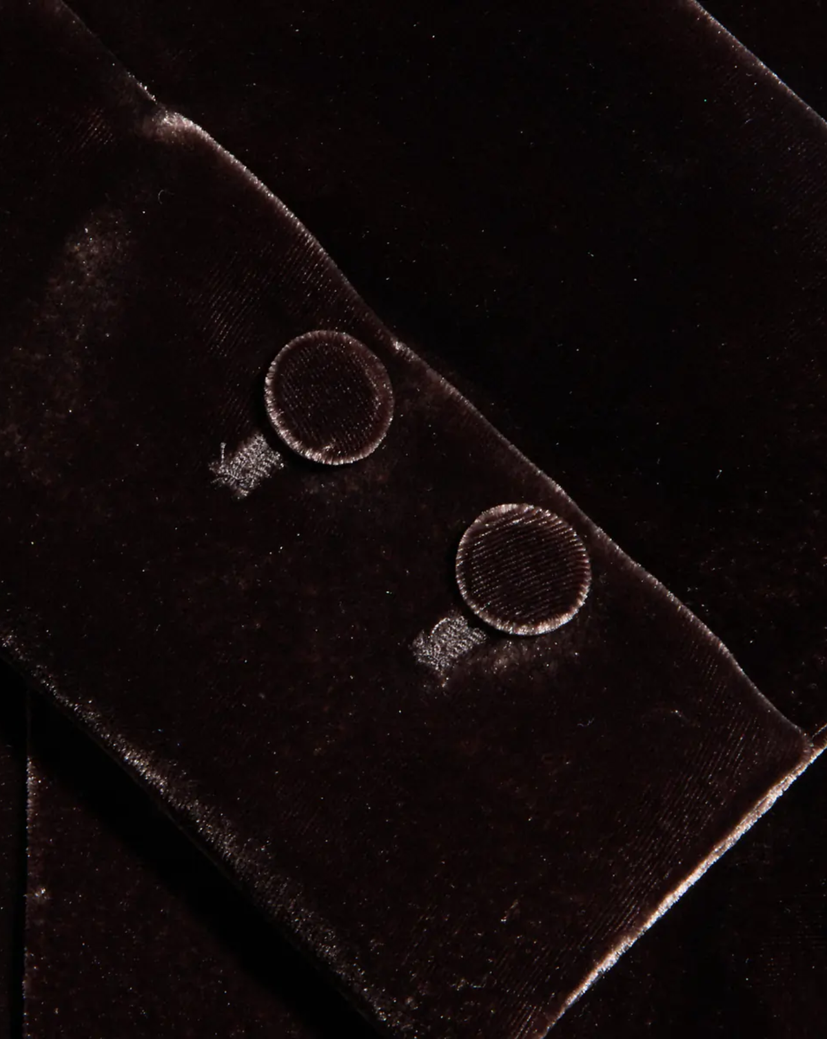 Close-up of a dark brown velvet garment detail showing two round buttons on a sleeve cuff.