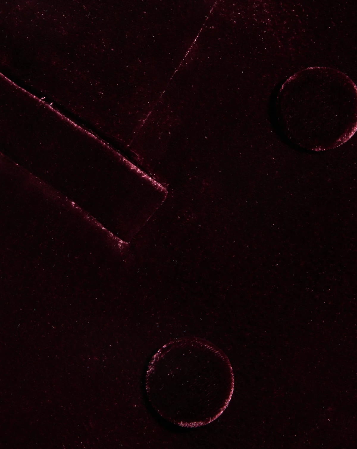 A close-up of a dark burgundy velvet fabric with a subtle sheen, showing the texture and a small portion of a matching garment or accessory.