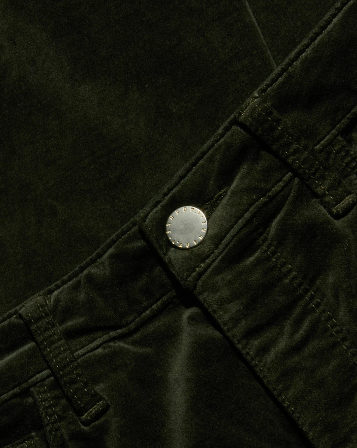 Close-up of dark olive green corduroy fabric with a silver-toned metal button closure.