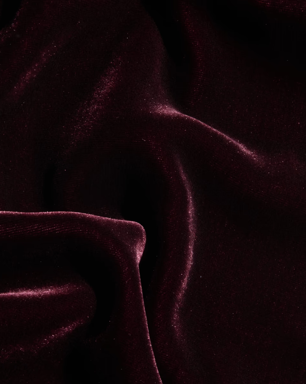 A close-up of draped deep burgundy velvet fabric with soft folds and a subtle sheen.