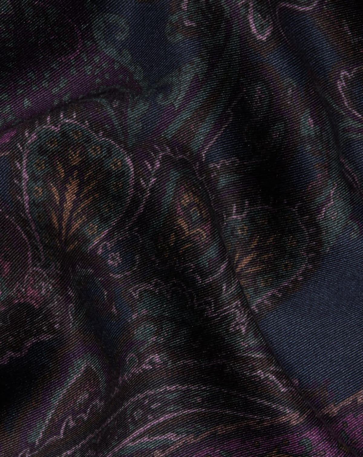 A close-up of a dark patterned fabric with a subtle paisley design in black, deep teal, and purple tones.