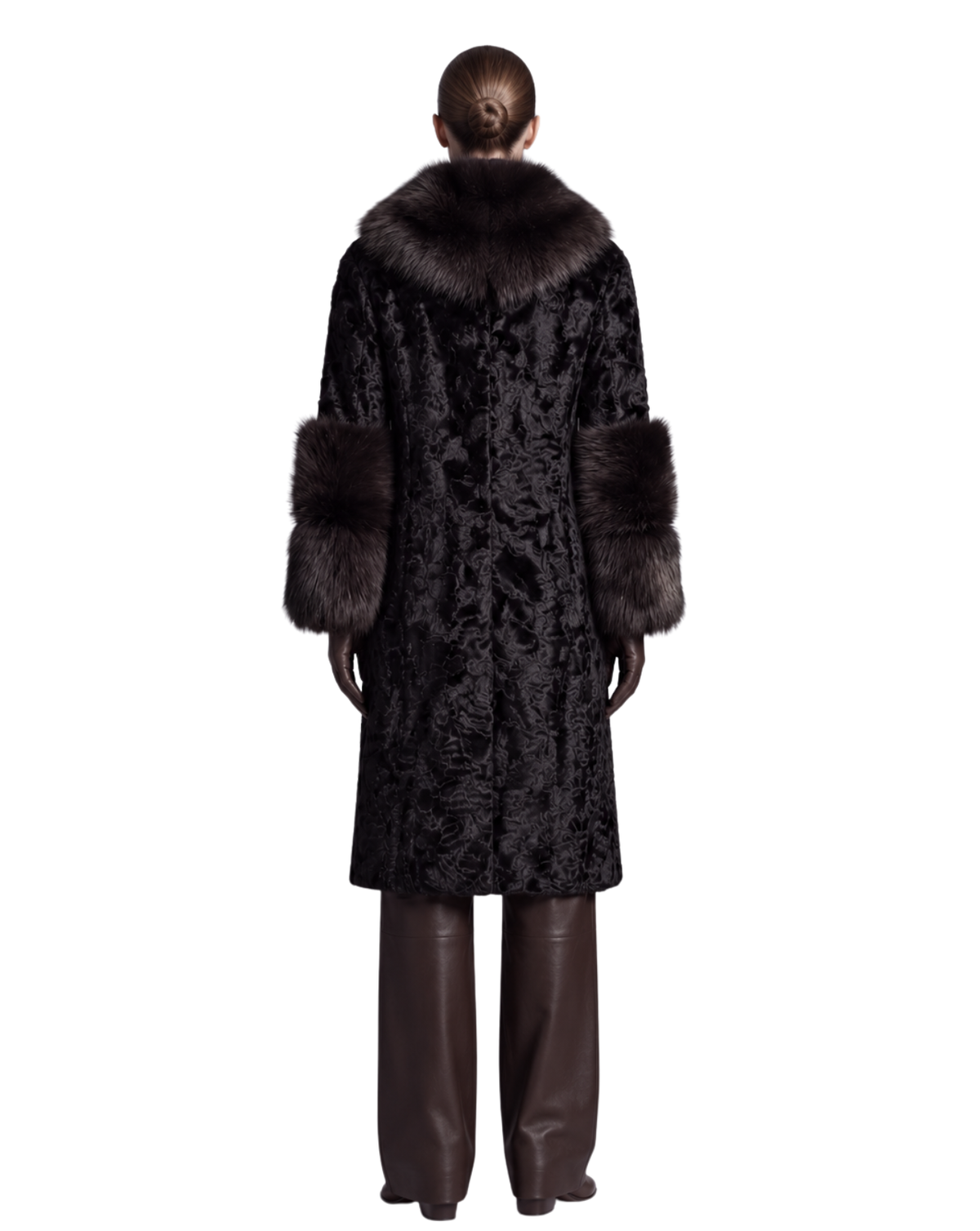 A model shown from the back wearing a long black patterned coat with a dark brown fur collar and cuffs, paired with dark brown leather pants, against a plain white background.