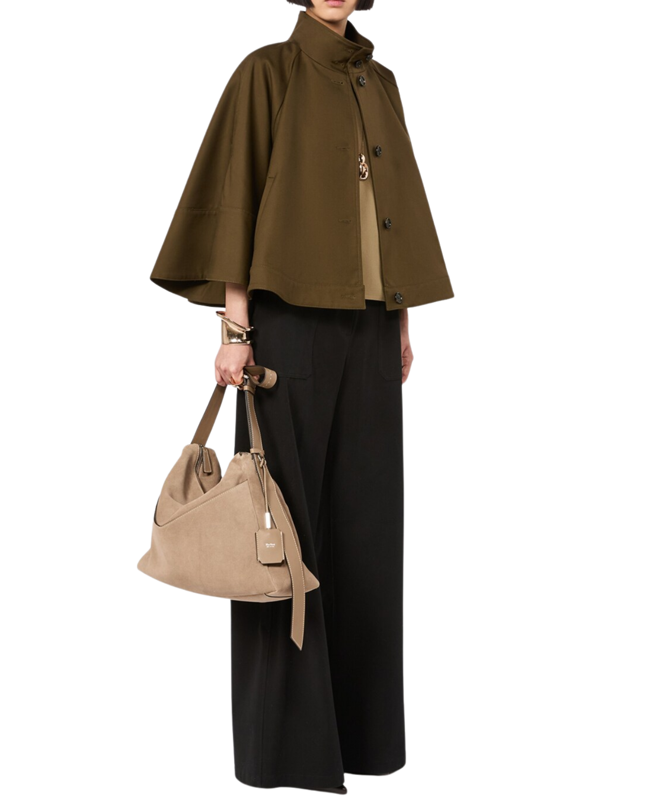 A model wearing an olive green cape jacket, black wide-leg trousers, and carrying a beige shoulder bag against a plain white background.