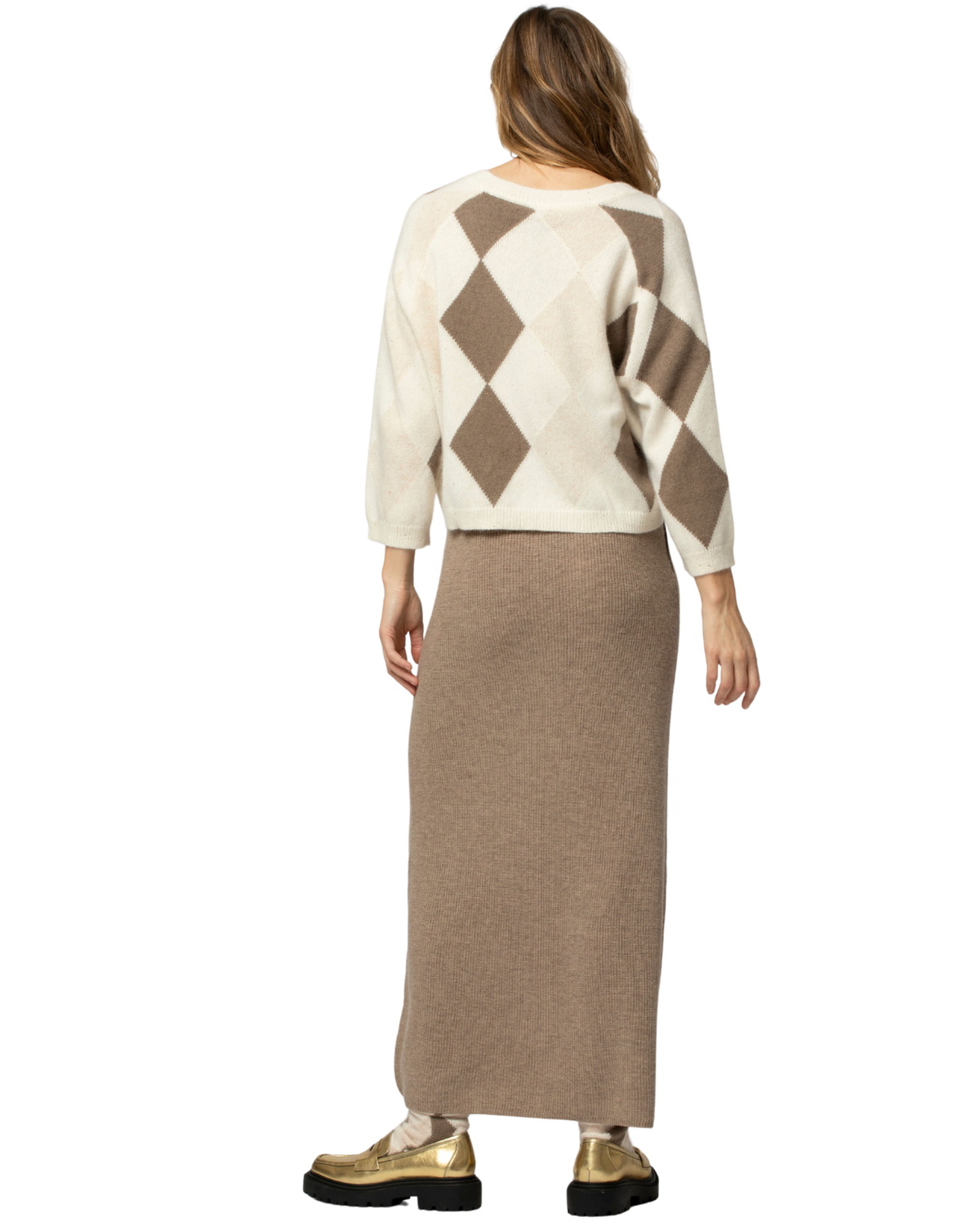A woman shown from the back wearing a cream and brown argyle sweater with three-quarter sleeves and a long taupe knit skirt, paired with gold shoes, against a plain white background.