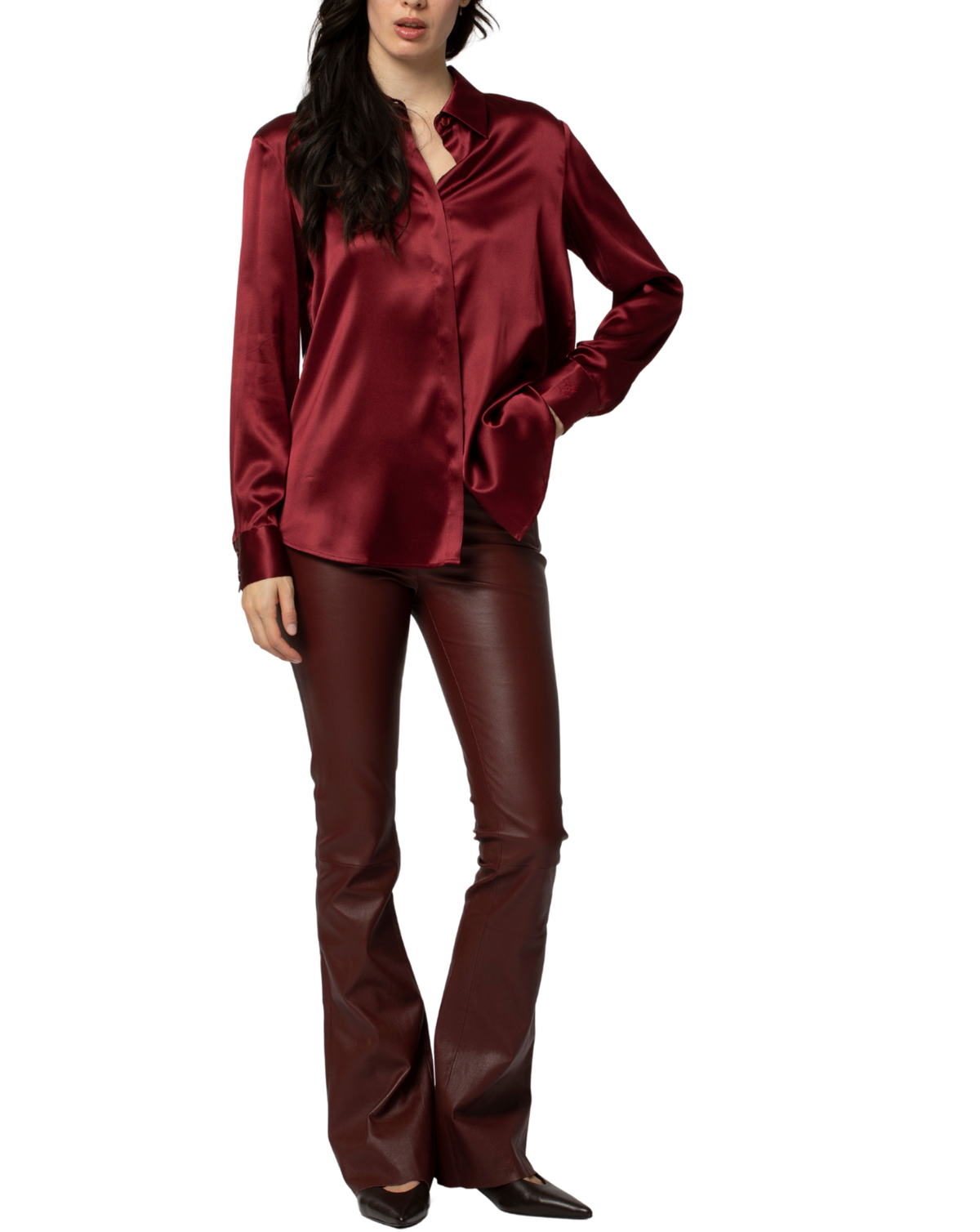 A woman modeling a matching burgundy satin button-up shirt and faux leather flared pants against a plain white background.