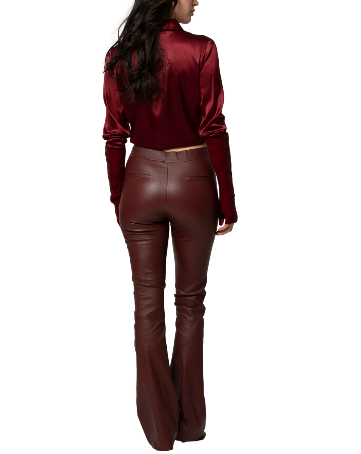 A woman shown from the back wearing a deep burgundy satin long-sleeve top and matching faux-leather flare pants against a plain white background.