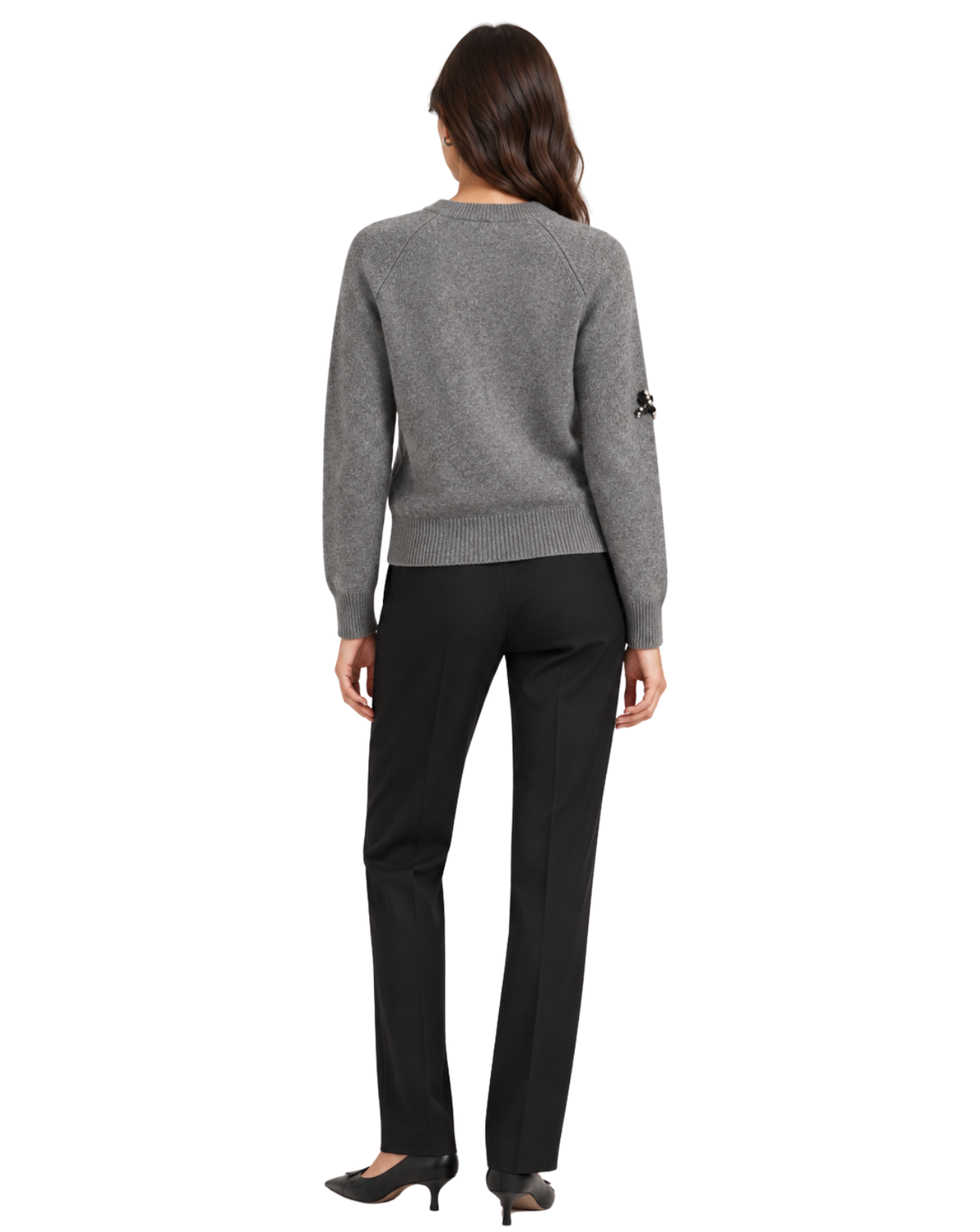 A woman viewed from the back wearing a heather gray knit sweater, black trousers, and black pointed-toe heels against a plain white studio background.
