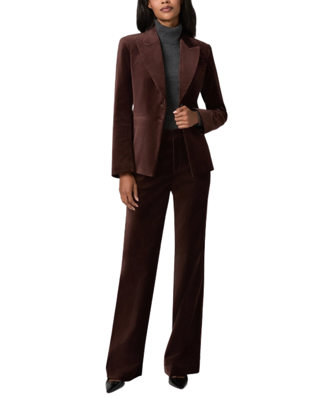 A model wearing a dark brown velvet two-piece suit consisting of a blazer and matching wide-leg trousers, styled over a gray turtleneck sweater and black pointed shoes, set against a plain white background.