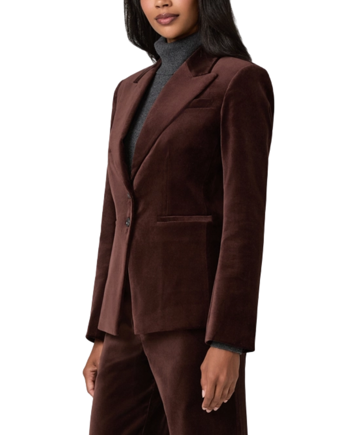 A woman wearing a dark brown velvet blazer and matching trousers over a gray turtleneck sweater, shown from the chest down against a plain white background.