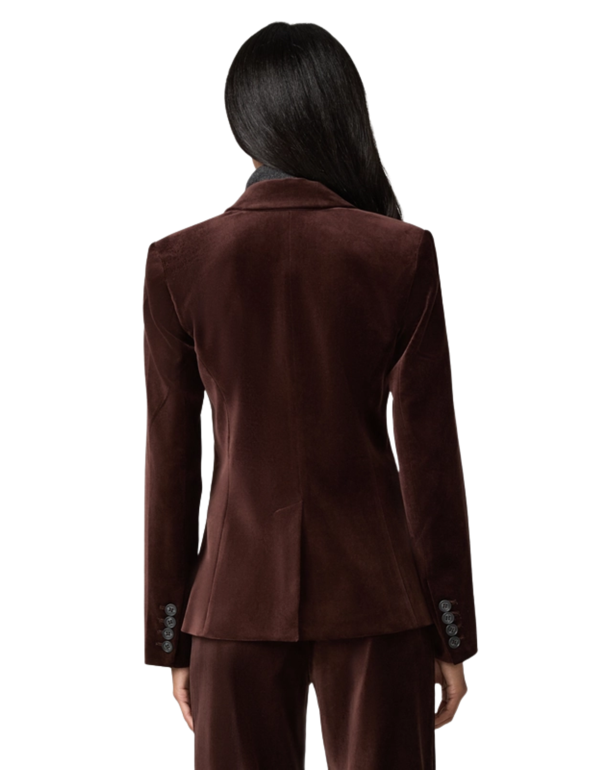 A woman viewed from the back wearing a dark brown velvet blazer and matching trousers against a light gray studio background.