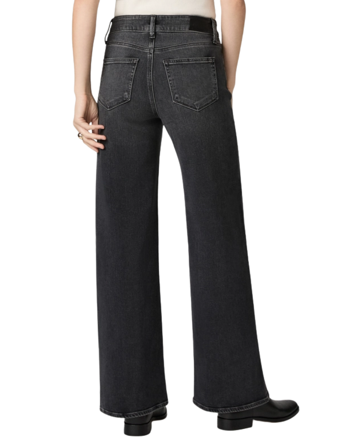 Rear view of a person wearing dark charcoal gray wide-leg jeans with a black belt and black boots, shown against a plain white studio background.