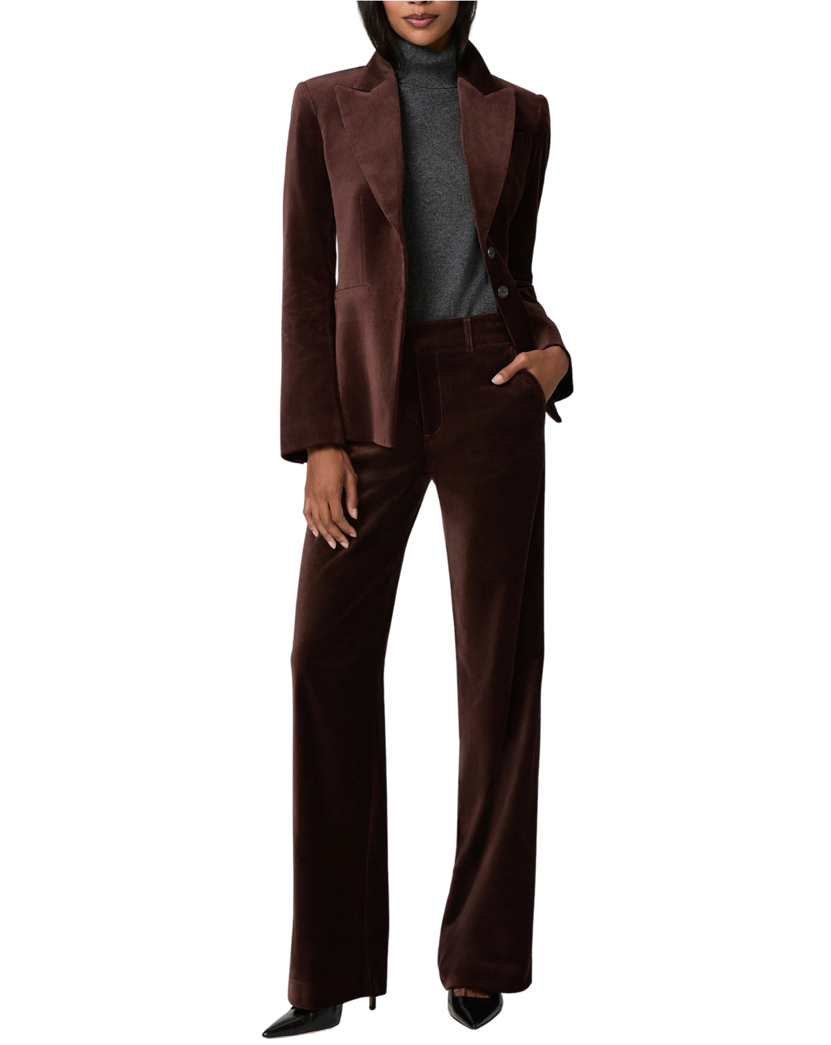 A model wearing a matching dark brown velvet pantsuit, consisting of a single-breasted blazer and wide-leg trousers, styled with a gray turtleneck and black pointed-toe heels against a plain white background.