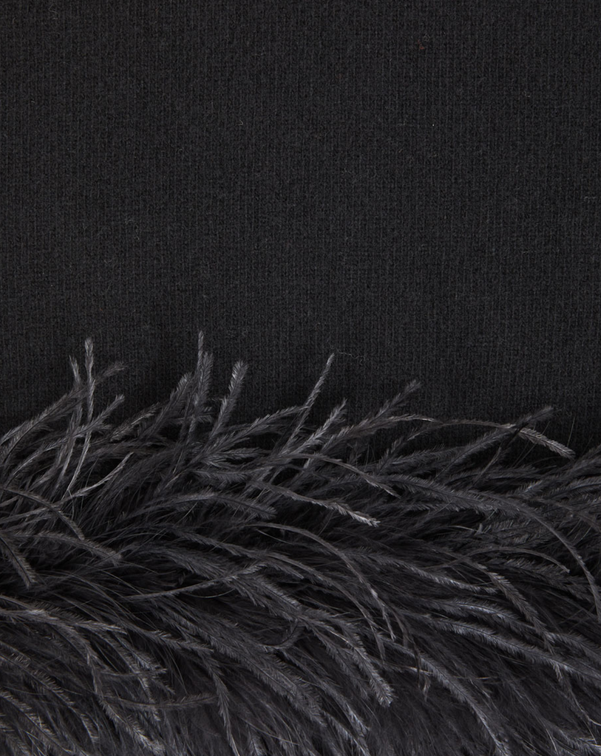 Close-up detail of a black knit garment with a black feather trim along the hem.