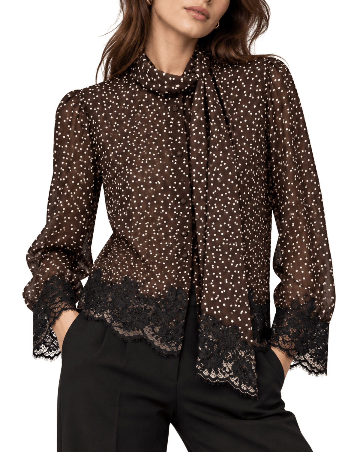 A woman wearing a sheer brown long-sleeve blouse with a white polka dot pattern, a high ruffled collar, and black lace trim at the hem and cuffs, paired with black pants against a white background.