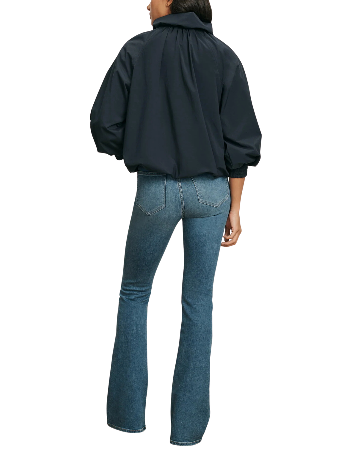 A model shown from the back wearing a dark navy blue cropped jacket with voluminous sleeves and blue flare jeans, set against a plain white background.