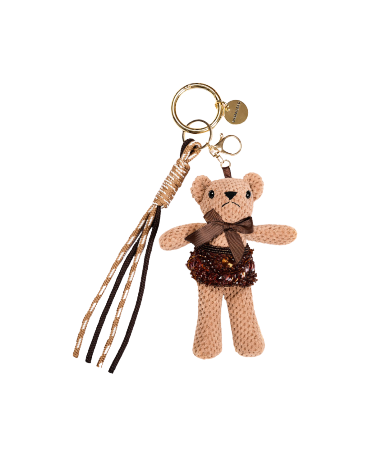 A teddy bear keychain charm with a beige knit body, brown sequined skirt, and brown ribbon bow, attached to gold-tone rings and a tassel with black and gold cords, on a plain white background.
