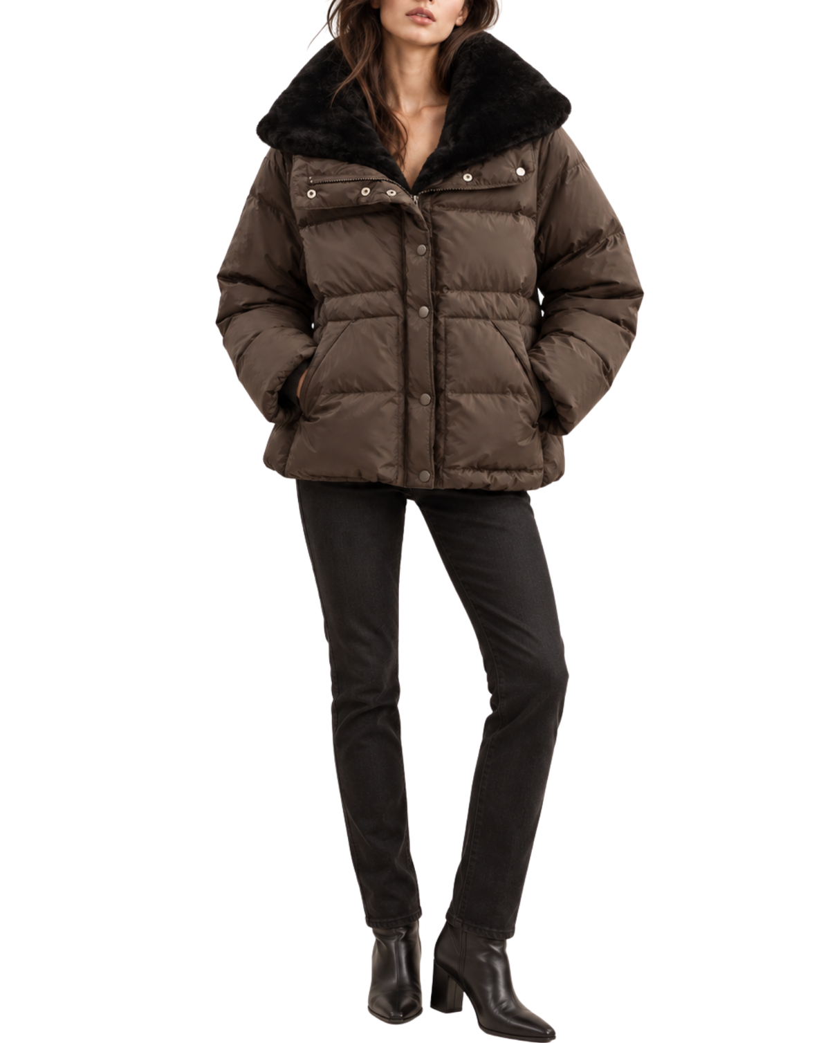 A woman modeling a dark brown puffer jacket with a black faux-fur collar, paired with black pants and black ankle boots, against a plain white background.