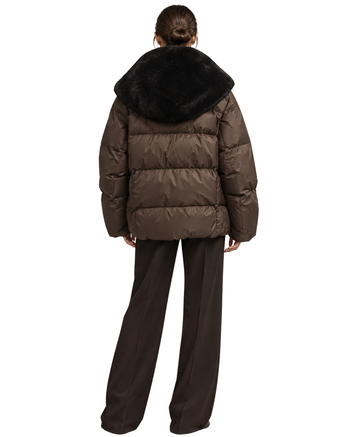 A model shown from the back wearing a brown puffer jacket with a large black faux-fur trimmed hood, paired with dark brown wide-leg trousers, against a plain white background.