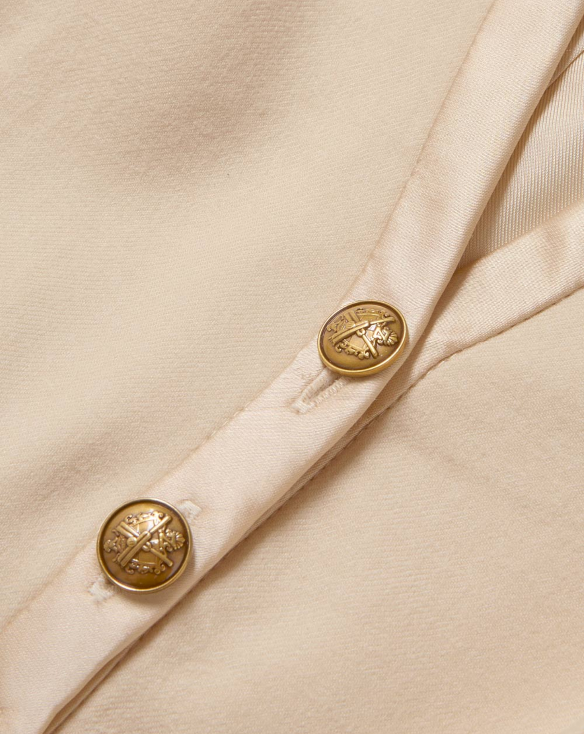 Close-up of a cream-colored fabric garment featuring two round gold-tone buttons with an embossed cross design.